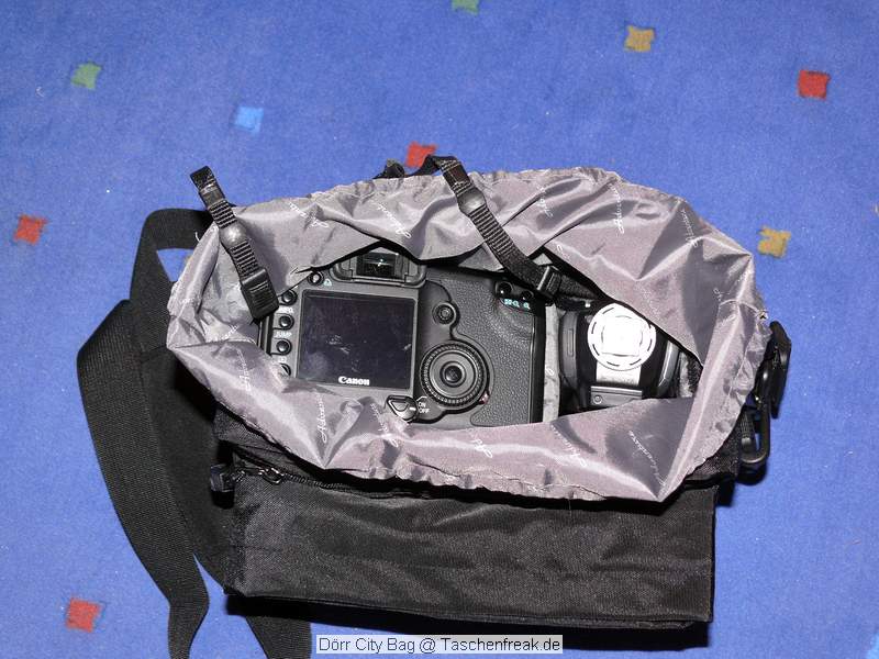 Dörr City Bag\n\nFoto von Jörg Langer\n\nKommentar des Nutzers:\n\nEine kleine Fototasche die nicht nach Fototasche aussieht und genau damit wird sie m.E. Ihrem Namen "City Bag" sehr gerecht.\n\nEs passen in dieses kleine Packwunder gut rein:\n\n- eine DSLR mit einem relativ großen Standardzoom wie einem 28-300er oder einem 18-200er oder ähnlichen Formfaktoren. Ein Canon 24-70 2,8L ist etwa 1 cm zu lang. In unserem "Packbeispiel hier haben wir ein 12-24 mit 82er Filterdurchmesser verwendet was deutlich größer ist als eins der genannten Reisezooms.\n\n- dazu eine 50er Festbrennweite und einen großen Systemblitz und Akkus dazu.\n\n- In die vielen kleinen und größeren Reisverschluss und Kletttaschen passen dann gut, Geldbörse, PDA, Handy und CF Cards sowie anderer Kleinkram rein.\n\nDier Tasche lässt sich sehr angenehm als Schulter- oder auch Torsotasche tragen.\n\nDer Preis ist mit 35 Euro vergleichsweise günstig und dadurch ist die Dörr City Bag auch gut als "Zweittasche" haltbar.\n\nDie Verarbeitung ist sehr hochwertig und sehr robust.\n\nDie Innentasche wird mit einem Kordelverschluss verzogen/verschlossen und dadurch ist die Cam auch relativ "Wasserfest" untergebracht.\n\nLeider passt auch das Equipment der Frau wie auf 2 Bildern zu sehen hervorragend hier rein, was den Innerfamiliären Konflikt "wer nutzt welche Tasche" nicht einfacher macht ;-)\n\nTaschenfreak Empfehlung: Sehr empfehlenswert!!!!