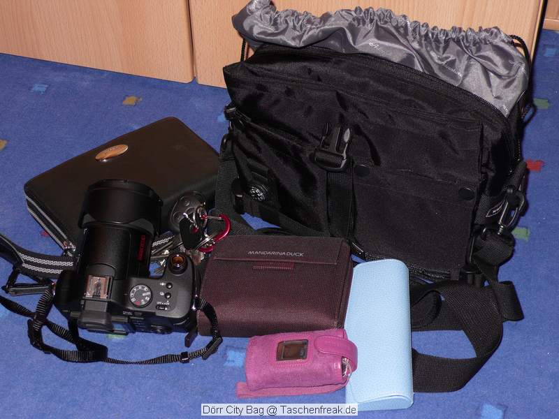Drr City Bag\n\nFoto von Jrg Langer\n\nKommentar des Nutzers:\n\nEine kleine Fototasche die nicht nach Fototasche aussieht und genau damit wird sie m.E. Ihrem Namen "City Bag" sehr gerecht.\n\nEs passen in dieses kleine Packwunder gut rein:\n\n- eine DSLR mit einem relativ groen Standardzoom wie einem 28-300er oder einem 18-200er oder hnlichen Formfaktoren. Ein Canon 24-70 2,8L ist etwa 1 cm zu lang. In unserem "Packbeispiel hier haben wir ein 12-24 mit 82er Filterdurchmesser verwendet was deutlich grer ist als eins der genannten Reisezooms.\n\n- dazu eine 50er Festbrennweite und einen groen Systemblitz und Akkus dazu.\n\n- In die vielen kleinen und greren Reisverschluss und Kletttaschen passen dann gut, Geldbrse, PDA, Handy und CF Cards sowie anderer Kleinkram rein.\n\nDier Tasche lsst sich sehr angenehm als Schulter- oder auch Torsotasche tragen.\n\nDer Preis ist mit 35 Euro vergleichsweise gnstig und dadurch ist die Drr City Bag auch gut als "Zweittasche" haltbar.\n\nDie Verarbeitung ist sehr hochwertig und sehr robust.\n\nDie Innentasche wird mit einem Kordelverschluss verzogen/verschlossen und dadurch ist die Cam auch relativ "Wasserfest" untergebracht.\n\nLeider passt auch das Equipment der Frau wie auf 2 Bildern zu sehen hervorragend hier rein, was den Innerfamiliren Konflikt "wer nutzt welche Tasche" nicht einfacher macht ;-)\n\nTaschenfreak Empfehlung: Sehr empfehlenswert!!!!