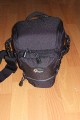 Foto von Jrg Langer\n\nKommentar des Nutzers:\n\nDie Toploader Serie von Lowepro ist sehr gut und hochwertig verarbeitet.\n\nIn dieses hier gezeigte Modell kann man Problemlos eine groe DSLR wie eine Canon 1D und ein All Round Zoom hineinpacken. Eine Schnellwechselplatte oder ein sogenannter L-Winkel passen auch geradeso noch hinein. Die Gegenlichtblende des Objektives sollte umgedreht montiert werden.\n\nIn der Vordertasche kann man entweder 2 groe Akkupacks oder einen mittelgroen Blitz reinpacken. Canon 420EX oder 430EX passen prima hinein, die groen 550EX oder 580EX sind etwa 1,5cm zu lang fr diese Vordertasche.\n\nAn den Seiten finden sie die Lowepro Sliplock Schlaufen an denen man gut seiten taschen oder eine Getrnkeflasche anbringen kann.\n\nIch setze hier gerne die LP D-Res25 an in der sich mein Polfilter udn 2 Akkupacks und ein paar Ersatzspeichercards befinden und auf der anderen Seite das kleine LP D-Res 8-S in dem sich meine Immerdabei Cam die Fuji F10 befindet.\n\nEine AW (Allwetterhlle) bzw. der Regenschutz befindet sich in der Fronttasche und kann auch wie abgebildet schnell und unkompliziert angebracht werden.\n\nFazit: Eine klasse Tasche fr das leichte "Sturmgepck". Bei mir gerne fr Feuerwehreinstze genutzt, weil ich da nichts auer meiner 1D und dem 24-105L und ab und zu einem kl. Blitz brauche.
