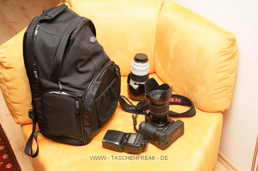 TAMRAC SPEEDPACK 3385\n\nFoto und Text von Johannes Waschke - VIELEN DANK!\n\nKommentar:\n\nHi!\n\nAnbei Bilder un Bericht zum o.g. Rucksack. Hoffentlich genügt es soweit Ihren Ansprüchen. Übrigens - klasse Website ;) !\n\nErläuterung:\n\n-Oben gibt es ein Fach für normales Gepäck. Dort passt zB. entweder ein Fußball rein, oder ein Sechserpack von 0,5l-Flaschen, oder eben im praktischen Einsatz Jacke und Pulli. \n-Unten liegt das Kamerafach: Canon 40D + BG + 17-55 + GeLi, 70-200 + (umgekehrter) GeLi, 2 Blitze passen locker rein. Ich würde behaupten, dass da noch ein mittelgroßes Objektiv (zB. 70-300er) reingeht. Man kann es ja auch sinnvoller packen als ich (das 70-200er hab ich hingestellt; man könnte es auch hinlegen - Hingestellt passt es gerade noch rein, sodass man allerdings schon eine leichte Beule außen am Rucksack hat) -Die Trennwand zwischen Gepäck- und Kamerafach ist enfernbar.\n-Echt fein: die Seitenöffnung! Da kann man die Cam aus dem Kamerafach nehmen, während man den Rucksack auf dem Rücken - oder zumindest an einer Schulter hängend- hat. Die 40D inkl. Batteriegriff passt mit leichtem Druck durch, sodass es eigentlich mit kaum einer Kamera Probleme geben dürfte. Viel größer sind ja auch die 1D etc. nicht.\n-Weitere Taschen: Außen ein Netz wo eine Trinkflasche reinpasst. Außerdem 2-3kleinere Fächer (Speicherkarten, Objektivdeckel,...)\n-Laptop-Tasche: Nutzen kann ich mangels Laptop nicht einschätzen.\n-Tragekomfort: Der Rucksack trägt sich sehr bequem; Größe ist gerade noch das, was ich auch auf Konzerten und ähnlichen Fotoveranstaltungen schleppen würde. Zum Wandern und verreisen ist es ideal!\n\nLiebe Grüße\nJohannes Waschke\n(www.johannes-waschke.de)