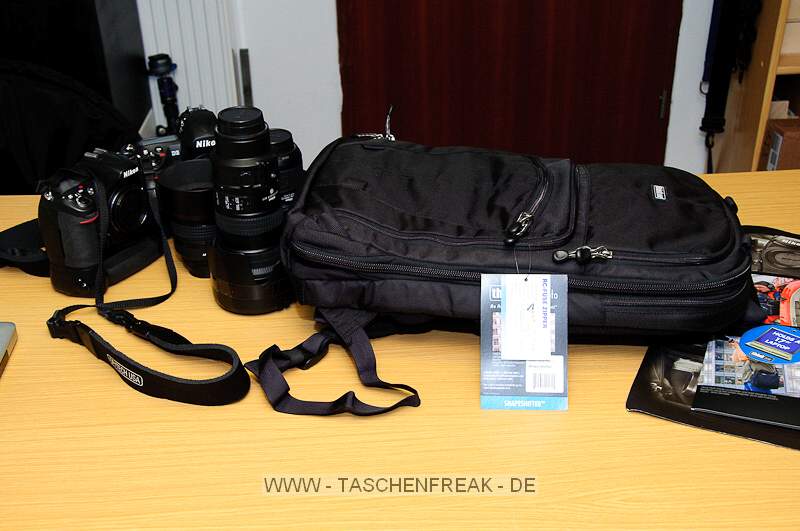 THINK TANK PHOTO - SHAPE SHIFTER\n\nFoto und Kommentar von Jörg Langer - www.taschenfreak.de\n\nKommentar:\n\nDer Shape Shifter, den wir freundlicherweise von ISARFOTO für einen Bericht und Test für Euch liebe Pagebesucher, zur Verfügung gestellt bekommen haben, löst bei uns den WOW Effekt aus.\n\nSehr schmal bzw. flach liegt er da auf dem Tisch und man fragt sich wie man das ganze Zeugs da rein bekommen soll ...\n\nLaut Hersteller sind 17" Notebook plus dessen Zubehör, 2x Profibodys, 3x 2.8er Profilinsen und jede Menge Zubehör kein Problem für dieses Teil.\n\nRECHT HAT ER DER HERSTELLER! Null Problem das alles darin zu verstauen und dennoch wirklich sehr bequem auf dem Rücken zu tragen.\n\nWas haben wir mal eben darin verstaut:\n\nBody D3\nBody D300 mit BG\n17-35 2.8\n24-70 2.8\n70-200 2.8\n85 1.4\nSB-900\nMBP 17" Unibody (wenn es eins gäbe würde auch ein 19" passen ...)\nNetzteil MBP, Maus, u.v.m.\n\nDie im Hauptfach beindlichen Neopren einzelhüllen sind grandios, sehr flexibel und dennoch hochschützend für das Equipment. Wir hatten vor einigen Monaten auch mal den Stealth Reporter II vom anderen großen Taschenhersteller - glaubt uns bitte - es liegen WELTEN dazwischen in der Verarbeitung des inneren und äußeren dieses Shape Shifters!\n\nWenn man das Fotofach nicht nutzt kann man den Rucksack als reinen Notebookrucksack mit einem umlaufenden Reissverschluss smarter und flacher machen - ein sicher sehr nützliches Detail wenn man Abends das ganze Fotozeugs im Hotel lässt und die Agentur oder die Kollegen mit dem Notebook aufsucht. \n\nJede Menge Kleinkram und persönliches was man so braucht und auch noch 2 weitere Blitze wären kein Problem - und das faszinierende: ES TUT NICHT WEH auf dem Rücken - der Shape Shifter bleibt sehr bequem und durch seinen eigentlich weichen Aufbau ist er sehr angenehm und nirgends störend auf dem Rücken - also auch während dem "Paparazzen" kann man diesen Rucksack aufbehalten.\n\nFazit: Wer Reportageartig fotografiert findet hier sein Werkzeug - ganz sicher!