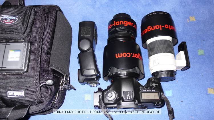 THINK TANK PHOTO - URBAN DISGUISE 30\n\nFoto von Jrg Langer - www.taschenfreak.de\n\nKommentar des Nutzers:\n\nDie Think Tank Photo Urban Disguise 30 ist unsere "Spaziergeh" und Sonntagsfototasche oder der ideale Begleiter fr den kleinen Stdtetripp am Wochenende.\n\nWir haben in diesem Beispiel in der von auen sehr klein und "smart" wirkenden Tasche untergebracht:\n\nCanon 5D mit L Winkel und angesetztem 24-70 2,8L inkl . umgedrehter Geli, einem 70-200 mit Stativschelle und umgedrehter Geli, einem 50 1,4 mit Geli und unserem groen 580er Blitz. In der Fronttasche sind dann CF Card Etui (Gepe Card Safe), und 2 Taschen fr Cam Akkus und Blitz Akkus). Platz fr Geldbrse und Handy ist auf jeden Fall noch und an der Rckentasche der Urban Disguise knnen auch noch bequem die Bahn oder Flugtickets verstaut werden.\n\nEin Regenschutz, ein bequemer (aber nicht strend groer und auffalender) Schultergurt und auch zwei sehr bequeme Handgriffe gehren auch zum Lieferumfang.\n\nDie Frontasche ist brigens so gro ausgelegt das man bequem einen 1D verstauen kann und dann im inneren der Tasche sogar ein 70-200 2,8 und ein 100-400 reinbekommt.\n\nEs sind die Feinheiten und die Details die man im Laufe der Zeit an den Think Tank Taschen zu schtzen lernt und dann merkt man auch warum die Taschen eventuell etwas teurer als "typische Consumer Fotoware" ist. Fragen sie einen Think Tank Anwender, er wei wir hiermit meinen.\n\nWie immer bei den Think Tank Produkten bekommt auch diese kleine Umhngetasche unser Prdikat "BESONDERS EMPFEHLENSWERT".