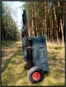 ZARGES TRANSPORTWAGEN - SELBSTBAU\n\nFoto und Text von Thomas Bder - VIELEN DANK!\n\nKommentar:\n\nTransport der Fotoausrstung\n\n \n\nNun ist es endlich soweit.\n\nLange habe ich an diesem Transportwagen geplant und gebaut.\n\nAuch wenn es vielleicht nicht so aussieht :-)\n\nBasis des Ganzen ist eine 60l Zarges Aluminiumkiste von der Bundeswehr.\n\nQuasi unkaputtbar und absolut wasserdicht.\n\nDie rckseitige Konstruktion besteht aus Aluminium und Eschenholz.\n\nHolz deshalb, weil es schn warm ist im Winter, man keine Schweihnde bekommt und Schlge gut abfedert werden.\n\nDie Eschenprofile sind als Nut und Feder ausgefhrt, damit man den Transportgriff ausziehen kann.\n\nIn die inneren Profile sind gefederte Bolzen eingebaut, die durch einen kleinen Seilzug nach innen gezogen werden knnen.\n\nDamit wird der Teleskopgriff entriegelt.\n\nDie weien Punkte an den Profilen, markieren die Einrastpositionen.\n\nUnten ist die Parkposition.\n\nNach oben hin gibt es Endanschlge aus Alu und Hartgummi, falls die Bolzen mal versagen sollten.\n\nDie luftgefllten Rder laufen auf einer 20mm Stahlrohrachse.\n\nDas blaue Beinchen unten, ist abschraubbar und nur fr den aufrechten Stand notwendig.\n\nBlau deshalb, um es im Ernstfall im Wald wiederzufinden ;-)\n\nAn einer Seite befindet sich die Halterung fr das Stativ.\n\nDieses Rohr hat unten ein eingeflochtenes Nylongarnnetz um das Stativ abzufedern und auch Wasser durchlaufen zu lassen.\n\nDie Stativhalterung ist innerhalb von Sekunden komplett abnehmbar, falls man kein Dreibein bentigt.\n\nDie beiden grauen Winkel mit den roten Kappen sind die Beine fr die liegende Position.\n\nIn der Box selbst gibt es zwei verstellbare Alutrennwnde.\n\nLinks und rechts befindet sich jeweils ein Einsatz einer Lowepro Stealth Reporter 500 AW Tasche.\n\nDiese 500er Taschen benutze ich normalerweise und kann somit wunderbar hin und her tauschen.\n\nIn der Mitte stehen einfach vier groe Objektivbecher nebeneinander.\n\nPlatz ist also mehr als genug...\n\nNun noch ein paar Daten:\n\nZum Zerlegen braucht man einen 4er und einen 6er Inbusschlssel, einen 13er Maulschlssel und einen normalen Kreuzschlitzschraubendreher.\n\nGewicht ca. 14kg also so ungefhr auf Pelicase Niveau nur mit dickeren Reifen :-)\n\nMae:\n\n60cm breit, 36cm tief, 73cm hoch (ohne Griff), mit ausgezogenem Griff 122cm\n\nInnenmae der Kiste:\n\n56cm breit, 37cm tief, 22cm hoch\n\nLink:\nhttp://www.makrofotografie.eu/index.php?option=com_content&view=article&id=47&Itemid=54